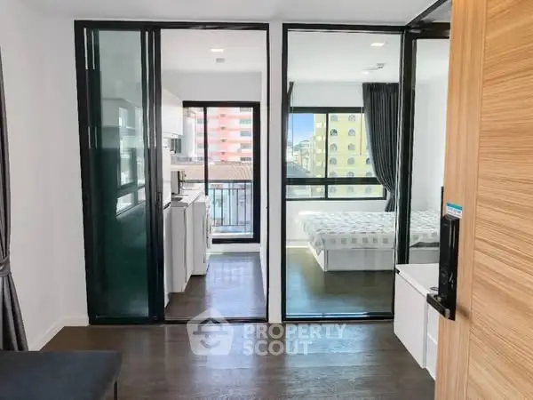 Modern apartment interior with glass partitions and city view, featuring bedroom and kitchen areas.