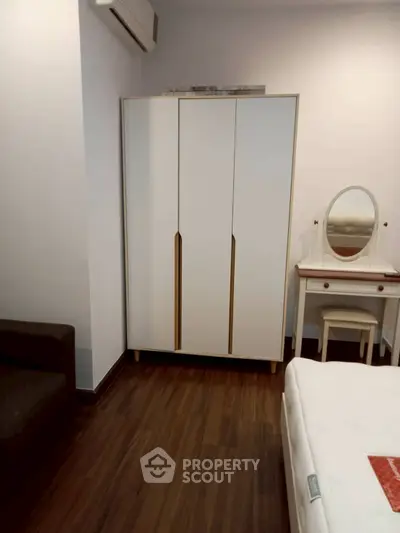 Cozy bedroom with modern wardrobe and vanity set, featuring elegant wooden flooring.