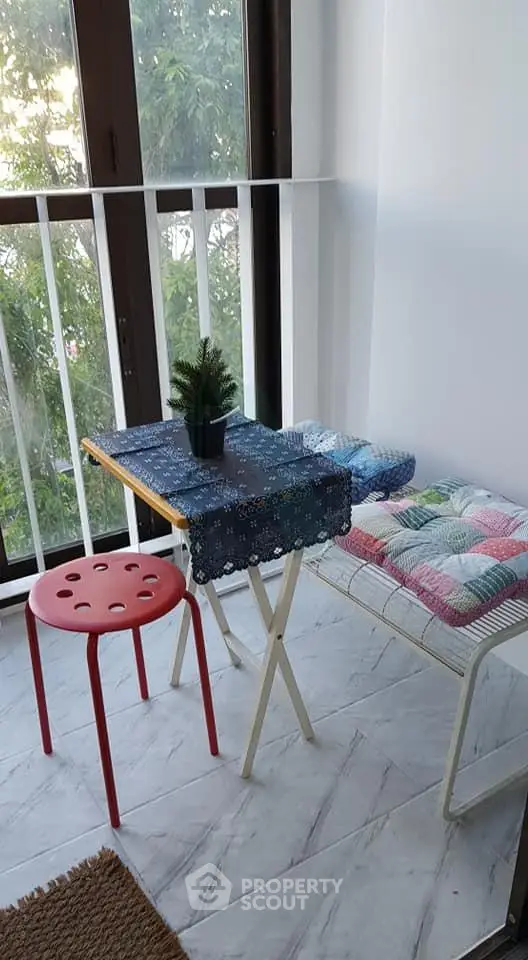 Cozy balcony with a small table, red stool, and potted plant, perfect for relaxation.