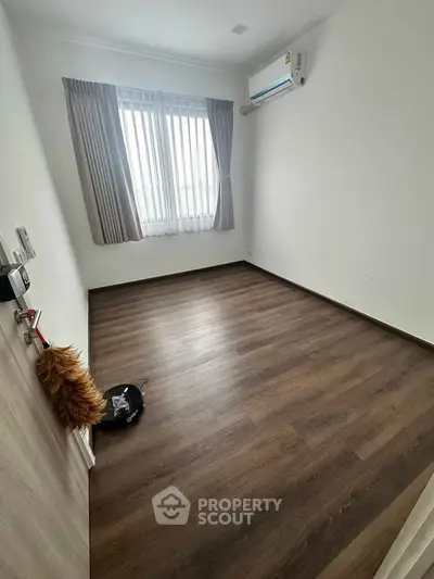 Spacious empty room with wooden flooring and large window, perfect for customization.