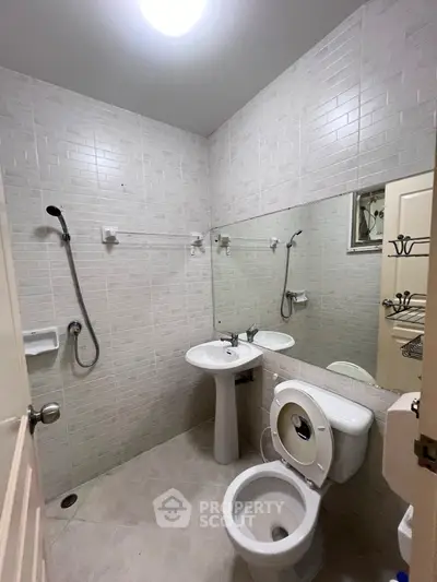 Modern bathroom with white tiles, pedestal sink, and shower area in a cozy apartment.