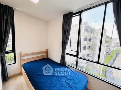 Bright bedroom with large windows and blue bedding, offering a city view.