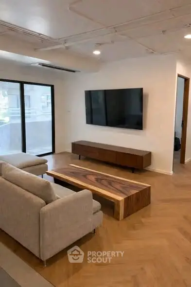 Modern living room with sleek furniture and large TV, featuring a stylish wooden coffee table and natural light.
