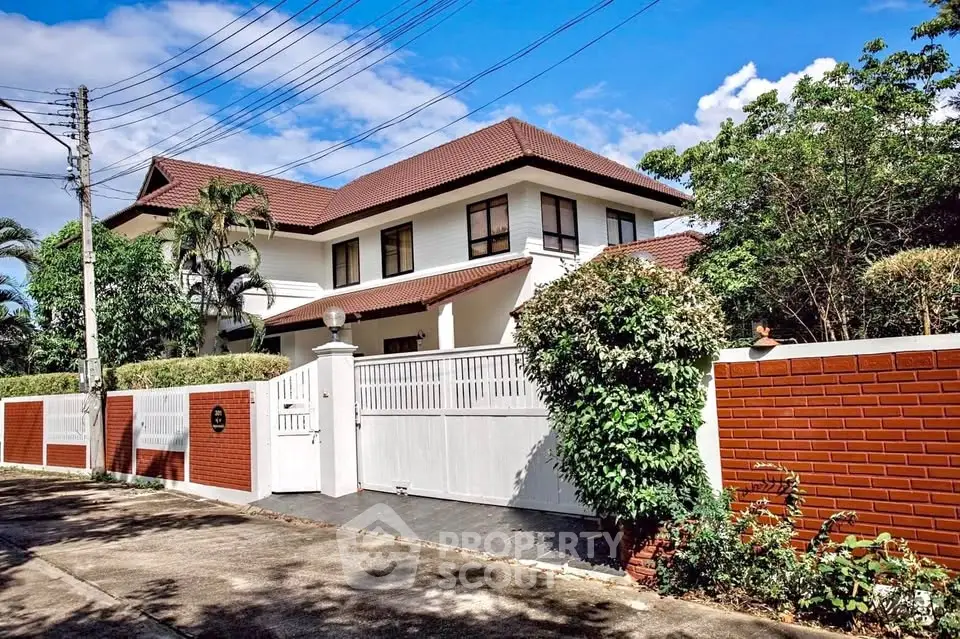 Charming two-story house with red brick fence and lush greenery, perfect for family living.