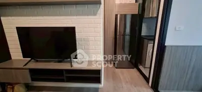 Modern living room with TV and adjacent kitchen featuring sleek appliances.