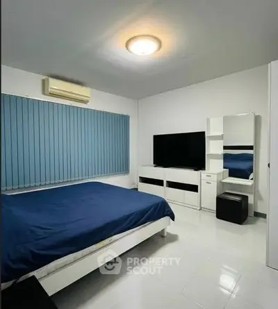 Modern bedroom with blue accents, featuring a sleek bed, TV, and stylish furniture.