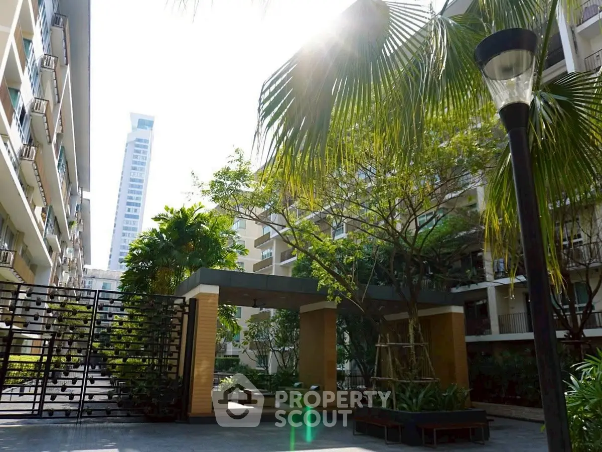 Modern apartment building with lush garden and sunlight filtering through palm trees.