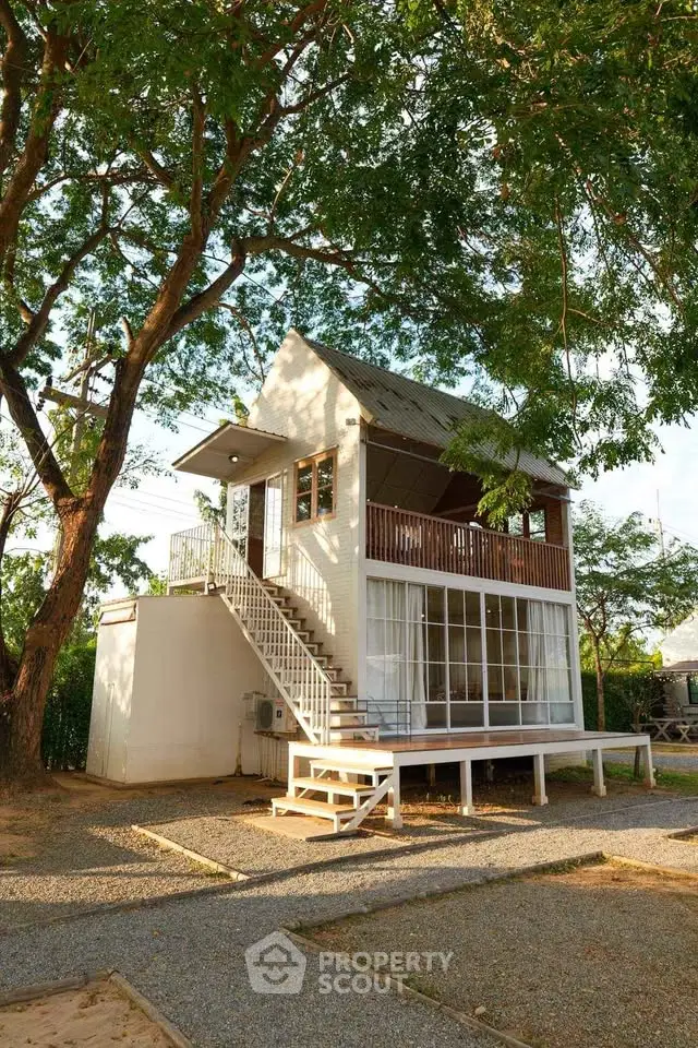 Charming two-story house with large windows and lush greenery, perfect for serene living.