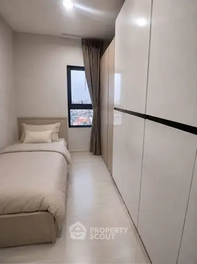 Cozy bedroom with single bed and large wardrobe, offering a serene city view through the window.