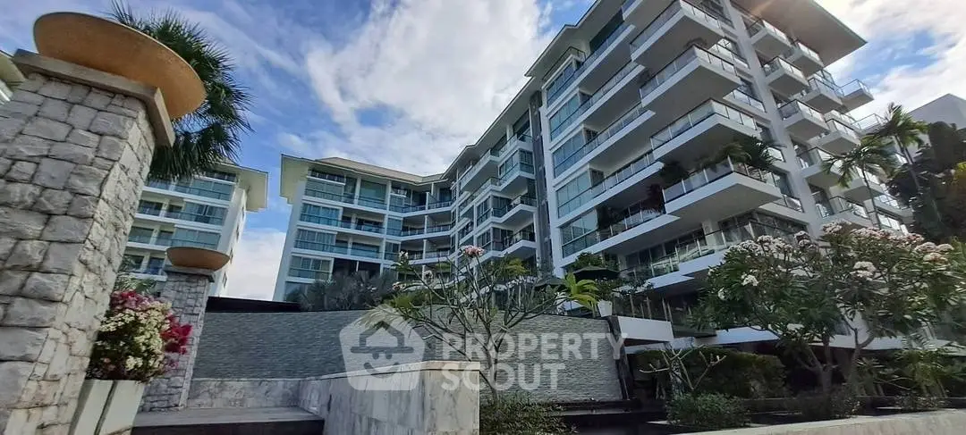 Modern multi-story residential building with lush landscaping and spacious balconies.