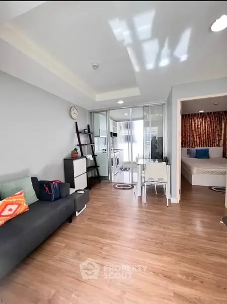 Modern living room with wooden flooring and glass partition leading to bedroom
