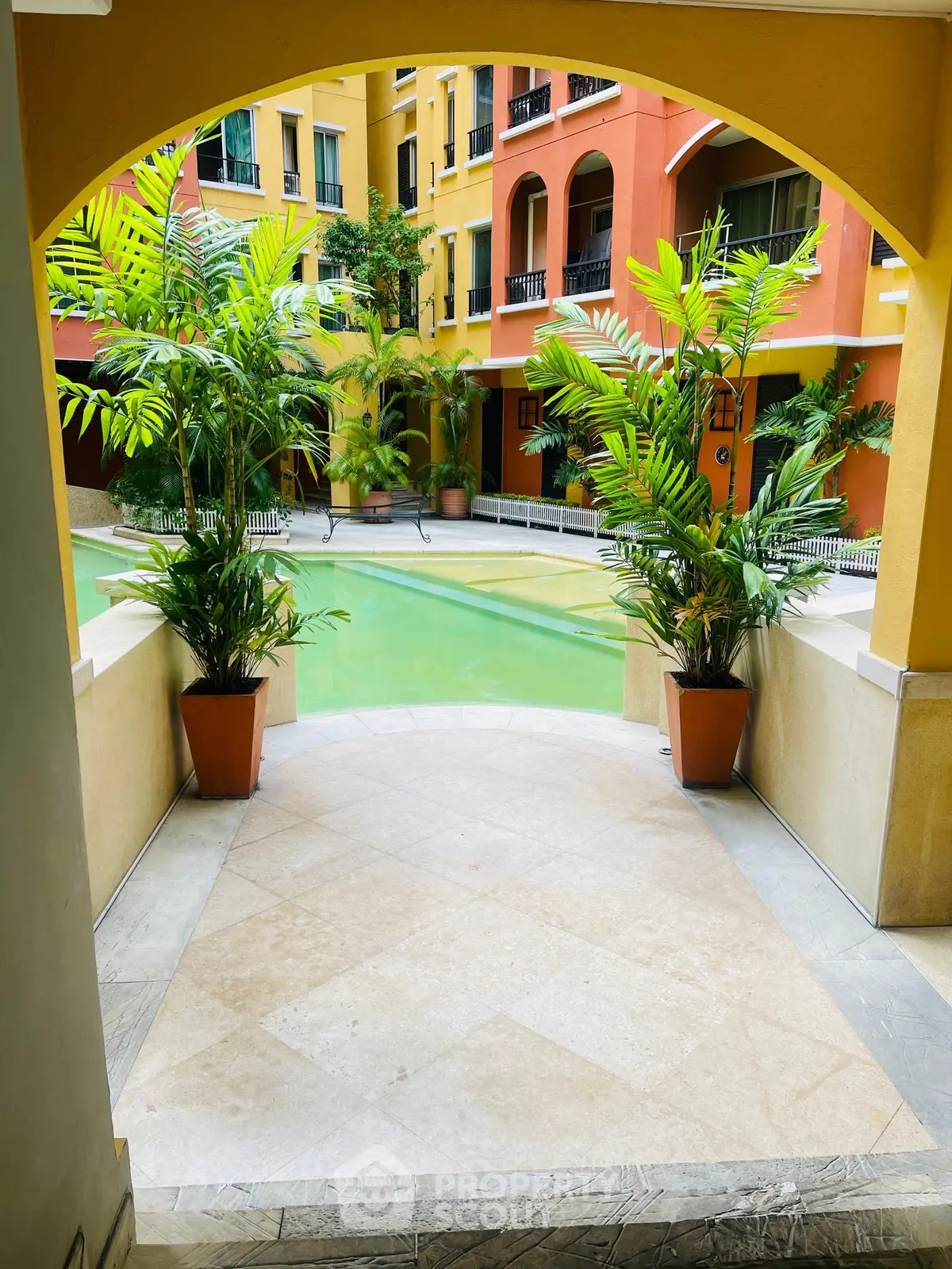 Charming courtyard view with lush greenery and inviting pool in vibrant residential complex.