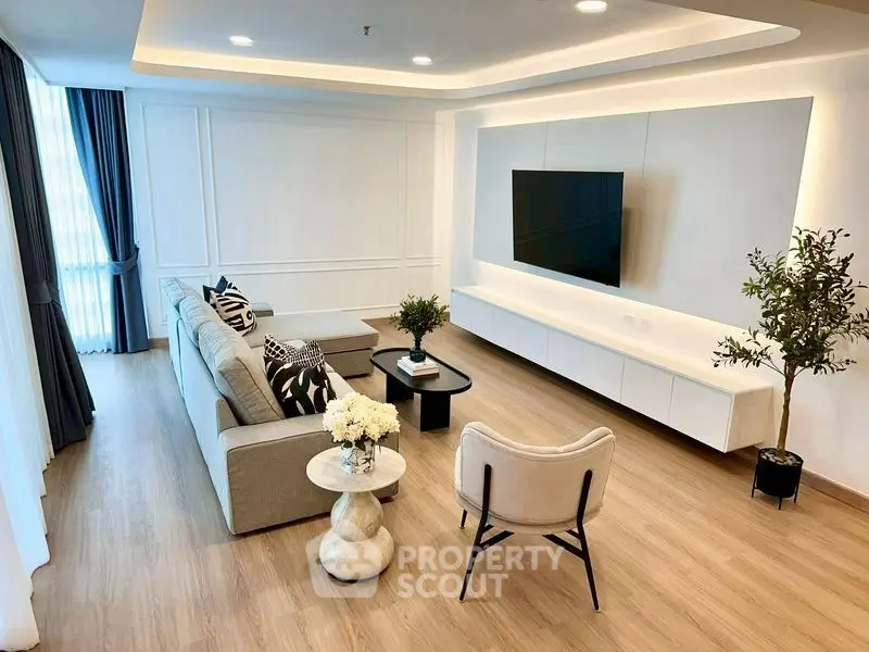 Modern living room with stylish decor and large wall-mounted TV, featuring elegant furniture and natural lighting.