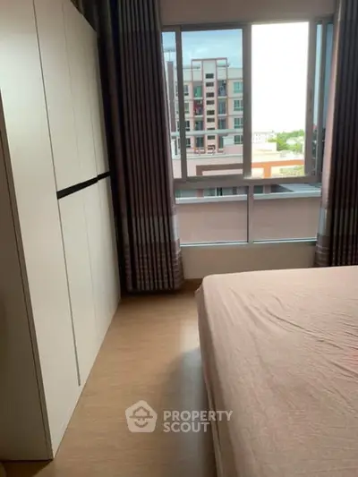 Cozy bedroom with large window offering city view and ample natural light.