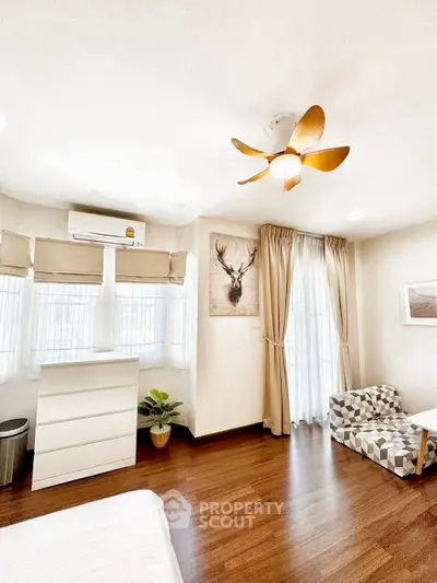 Bright bedroom with wooden flooring, stylish ceiling fan, and cozy seating area.