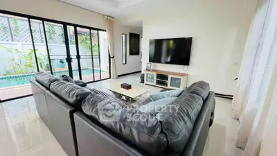 Spacious living room with pool view, featuring modern leather sofa and large TV, perfect for relaxation.