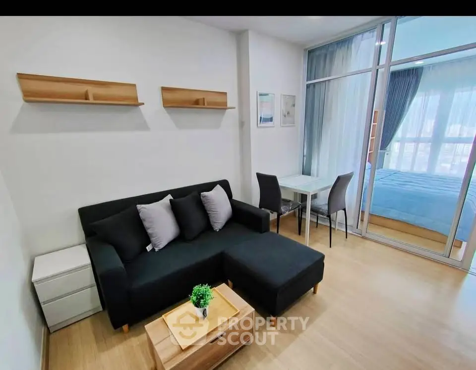 Modern living room with black sofa, wooden flooring, and glass partition leading to a bedroom.