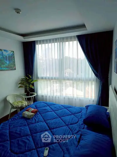 Cozy bedroom with large window and blue bedding, offering natural light and serene ambiance.