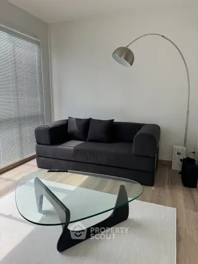 Modern living room with sleek black sofa and stylish glass coffee table, featuring a contemporary floor lamp.