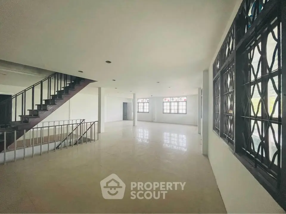 Spacious open-plan living area with large windows and staircase, ideal for modern living.