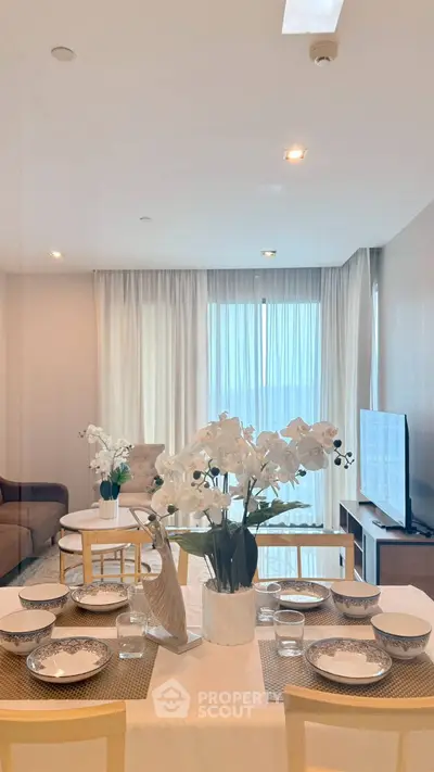 Elegant living room with dining area, modern decor, and large windows offering natural light.