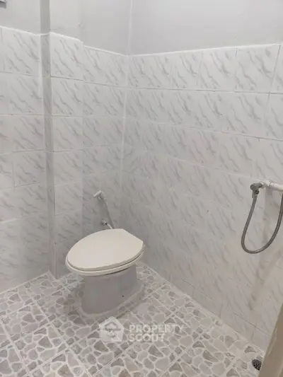 Simple bathroom with tiled walls and floor, featuring a toilet and bidet spray.
