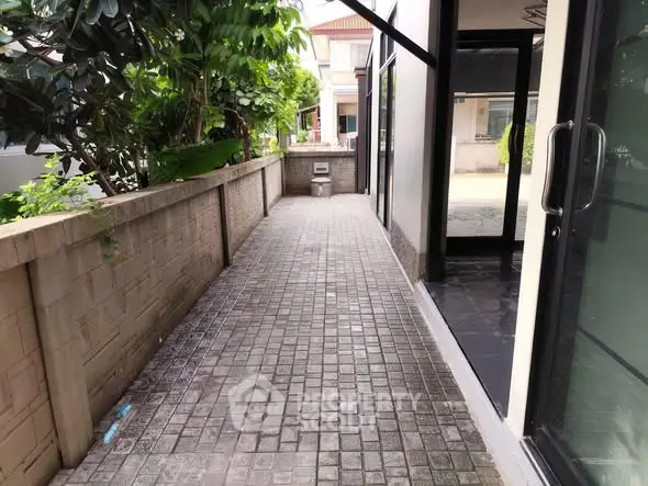 Charming exterior walkway with lush greenery and modern glass doors.