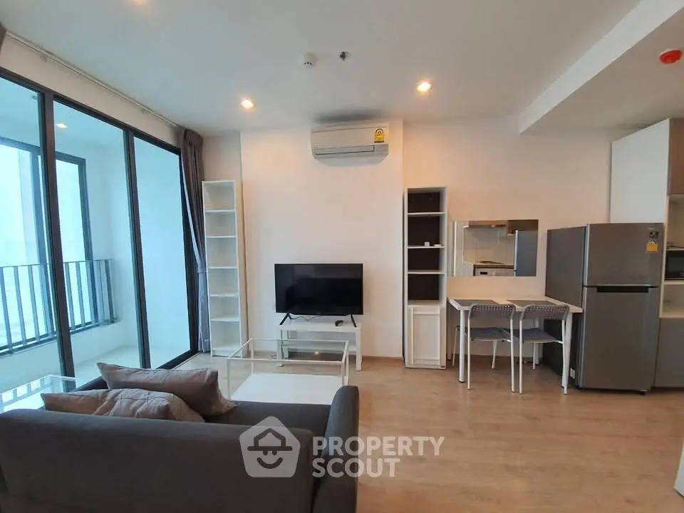 Modern living room with balcony, sleek furniture, and open kitchen layout in a stylish apartment.