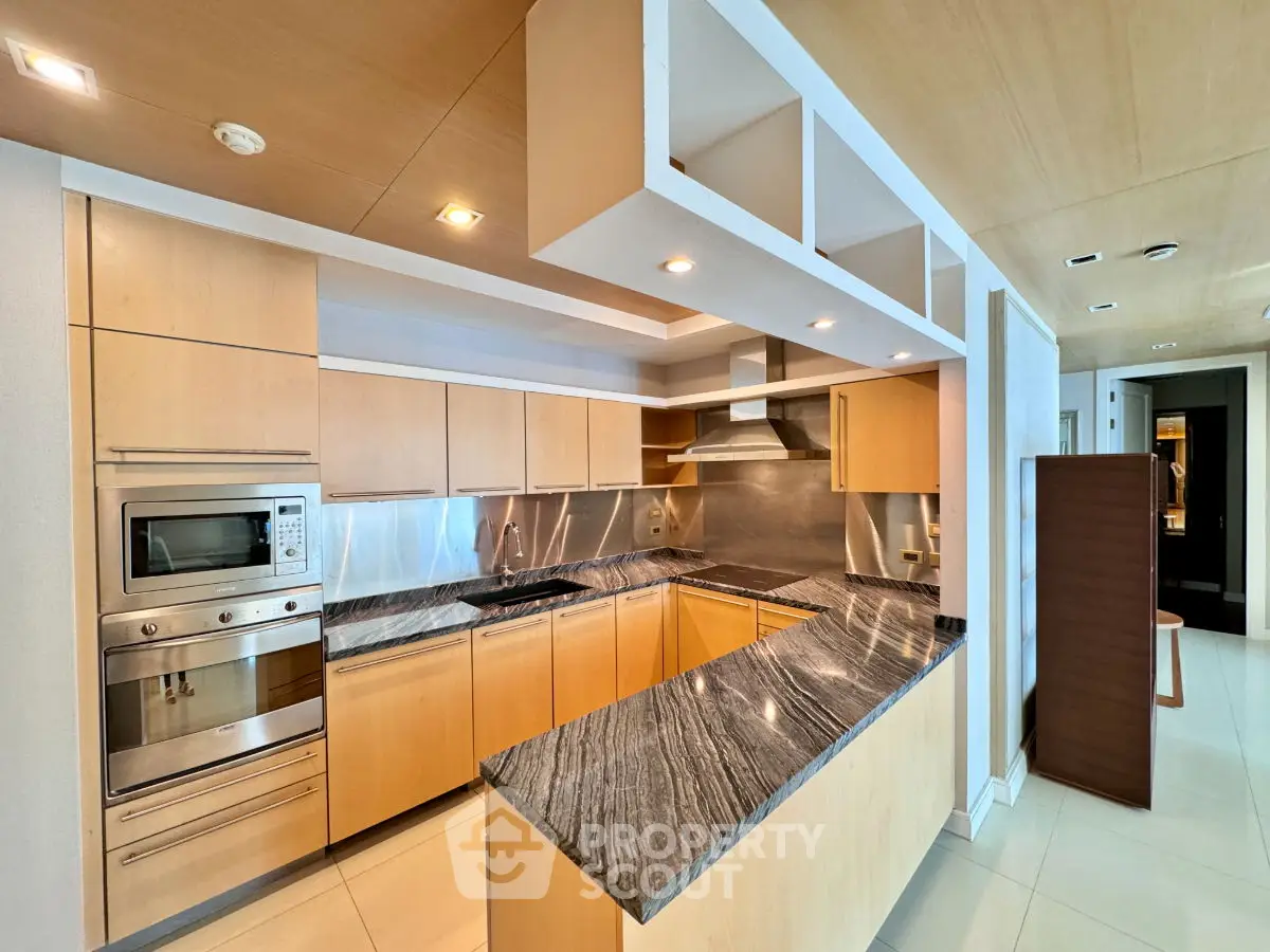 Modern kitchen with sleek wooden cabinets and marble countertops, featuring built-in oven and stylish lighting.