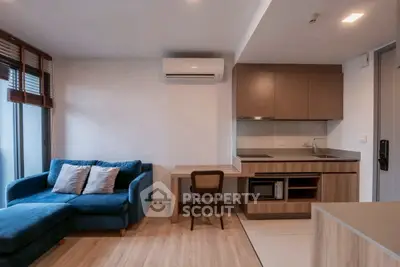 Modern living room with blue sofa, compact kitchen, and wooden flooring in a stylish apartment.
