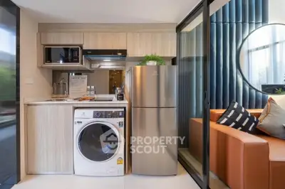 Modern compact kitchen with washing machine and fridge next to cozy living area