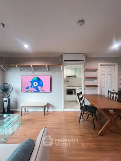 Modern living room with wooden flooring, wall-mounted TV, and dining area leading to a compact kitchen.