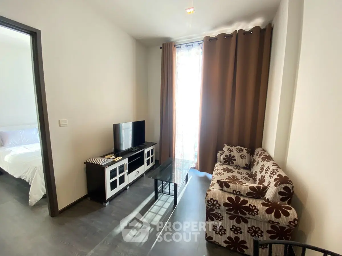 Cozy living room with floral sofa and TV, adjacent to a bright bedroom.