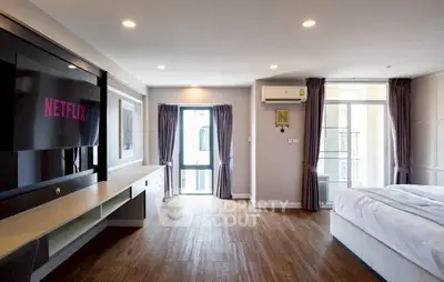 Spacious modern bedroom with wooden flooring and large TV, perfect for relaxation.