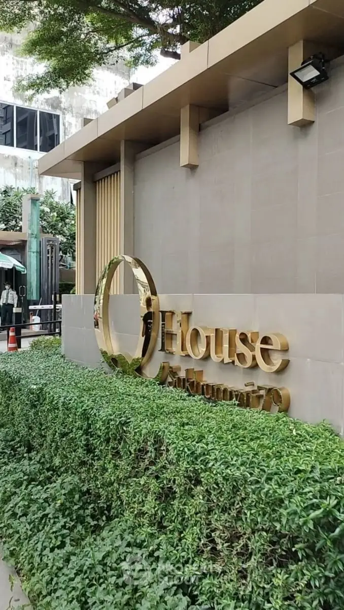 Elegant entrance of a modern building with lush greenery and stylish signage.