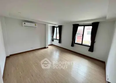Spacious empty room with wooden flooring and large windows, perfect for customization.