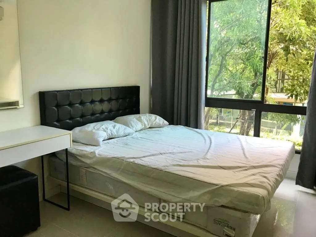 Spacious bedroom with large window and modern furnishings, offering a serene view of lush greenery.