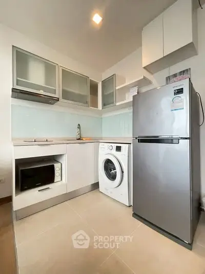Modern kitchen with sleek appliances including fridge, washing machine, and microwave in a compact layout.
