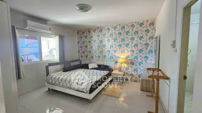 Spacious bedroom with stylish wallpaper and natural light, featuring a cozy bed and modern decor.