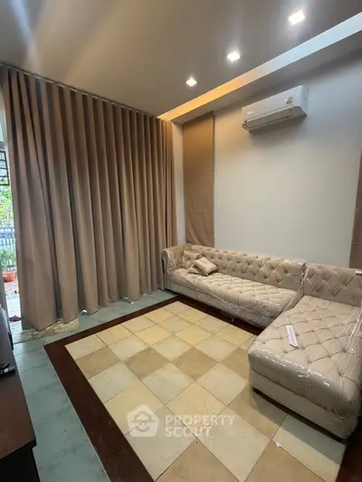 Spacious living room with elegant sofa and large window draped with curtains, featuring modern air conditioning.