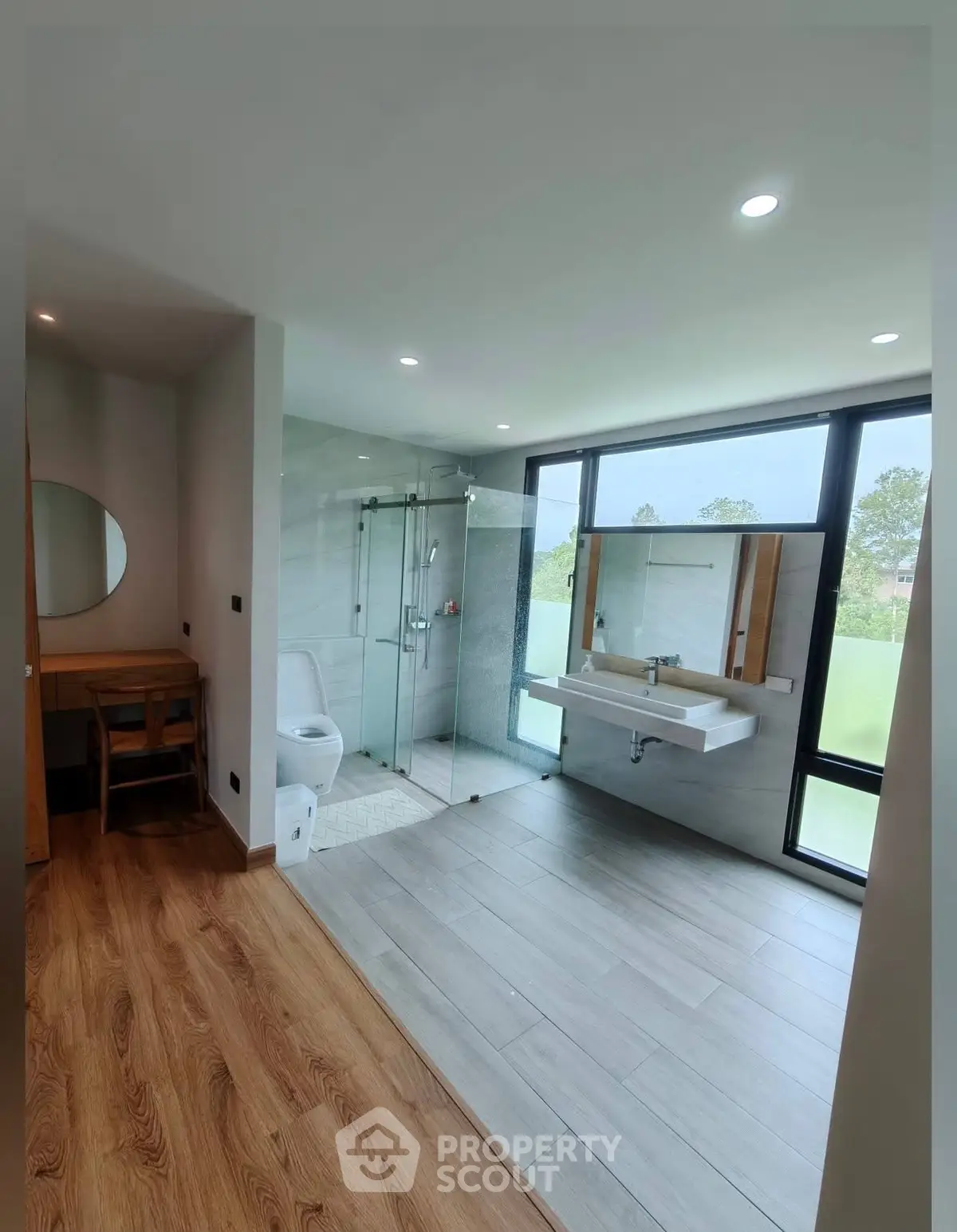 Modern bathroom with glass shower and large windows offering natural light.