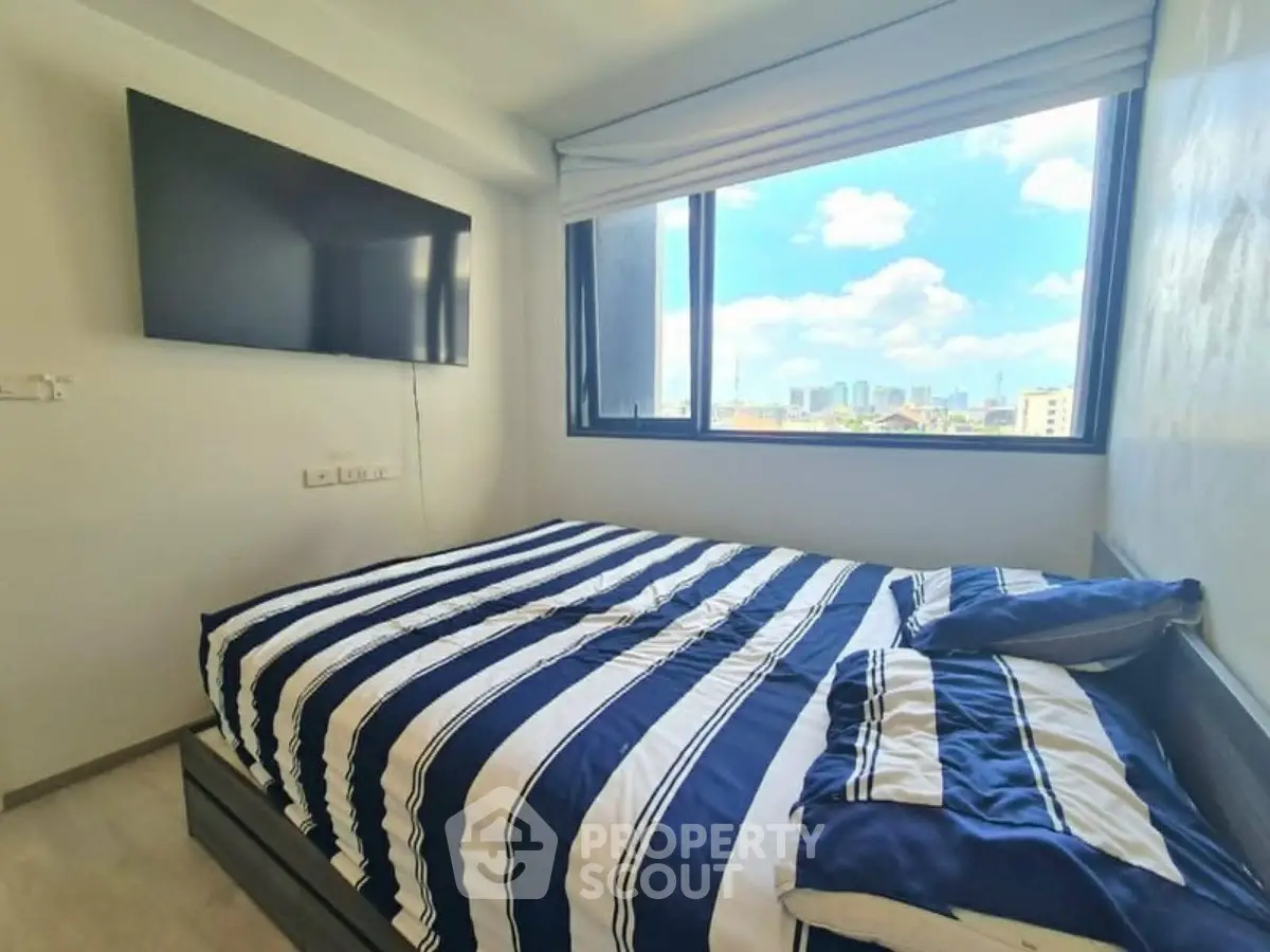 Modern bedroom with large window offering stunning city views and wall-mounted TV.