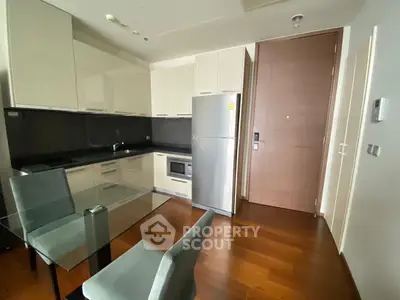 Modern kitchen with sleek cabinets, glass dining table, and stainless steel appliances in a cozy apartment.