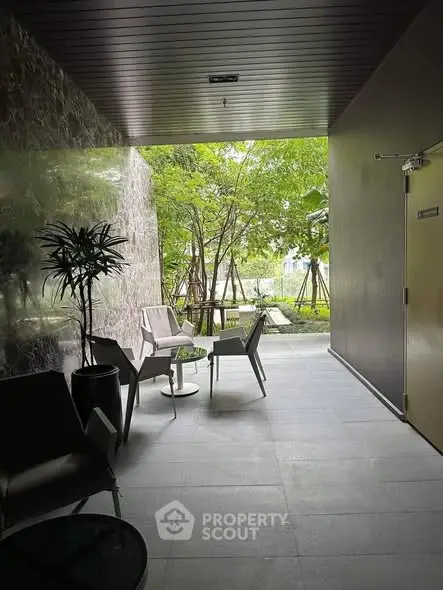 Modern building entrance with stylish seating and lush greenery view.