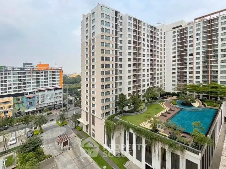 Modern high-rise building with rooftop pool and lush greenery in urban setting.