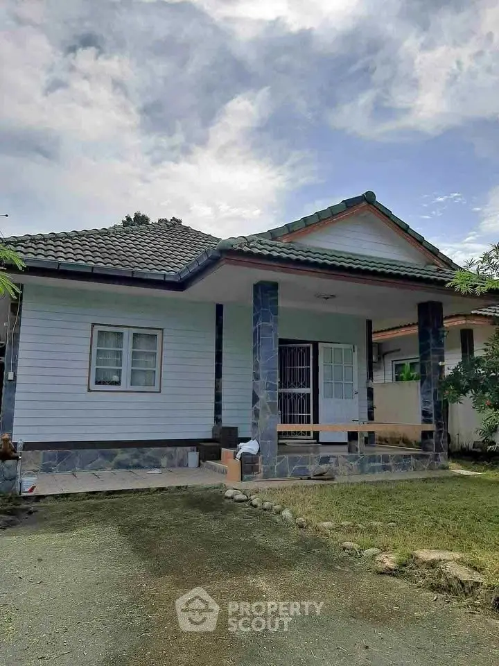 Charming single-story house with tiled roof and spacious front yard under a clear blue sky.