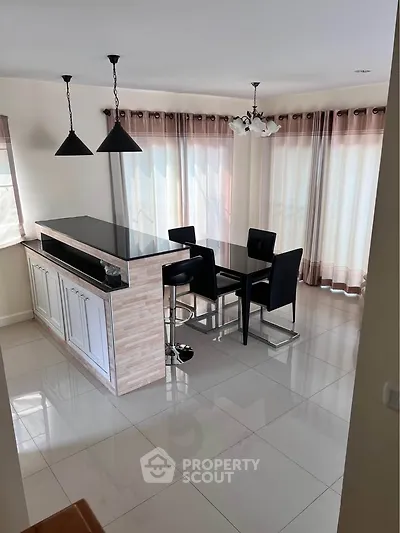 Modern kitchen with open layout and stylish dining area, featuring sleek black countertops and elegant lighting.