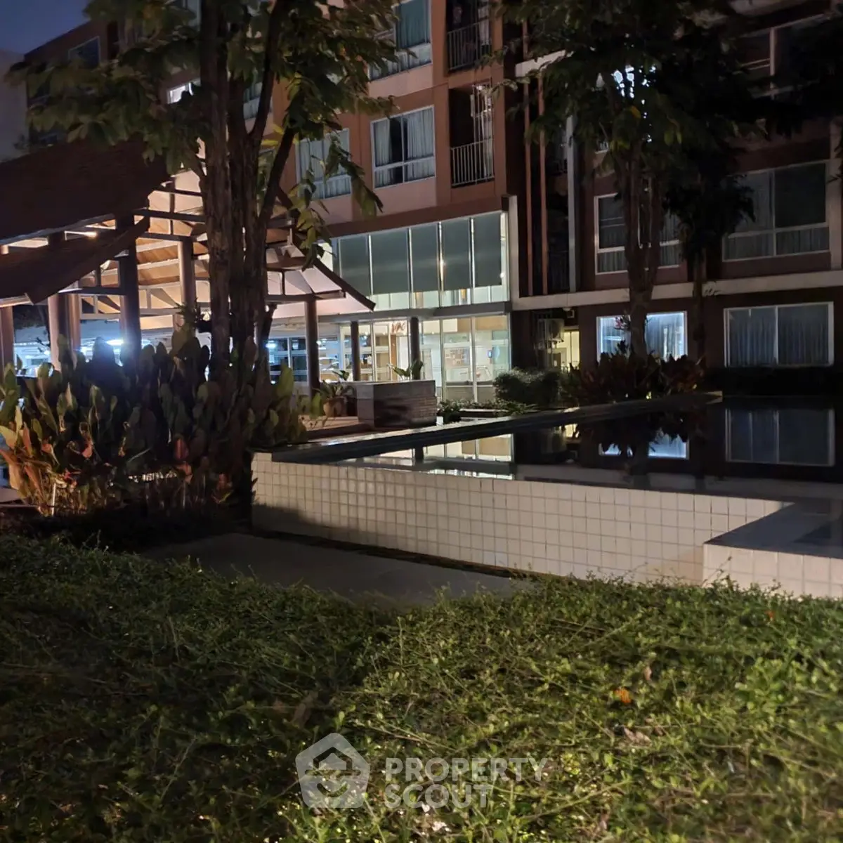 Modern apartment complex with pool and lush greenery at night, offering serene living environment.