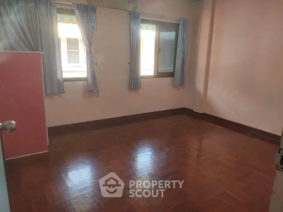 Spacious empty room with wooden flooring and natural light from two windows.