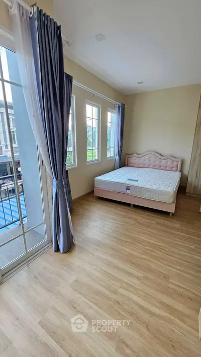 Spacious bedroom with large windows and elegant curtains, featuring a comfortable bed and wooden flooring.